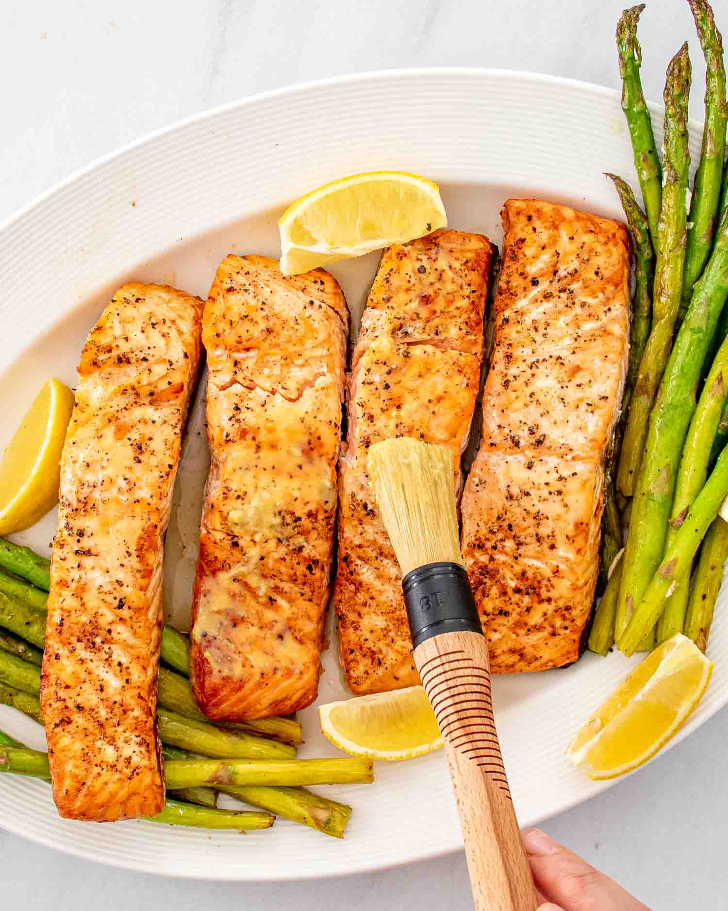 air fryer salmon and asparagus on a white platter with a lemon sauce.