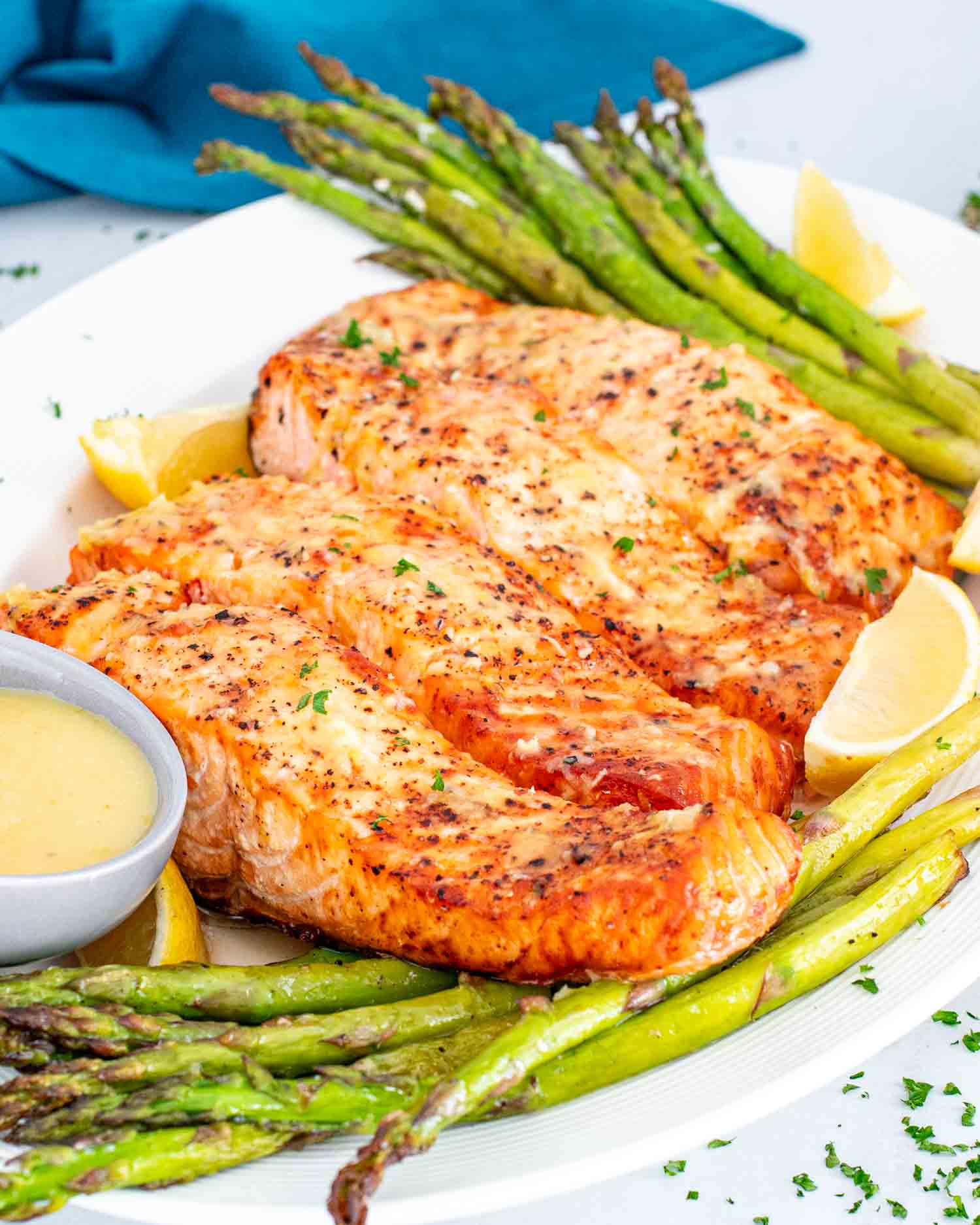 air fryer salmon and asparagus on a white platter with a lemon sauce.