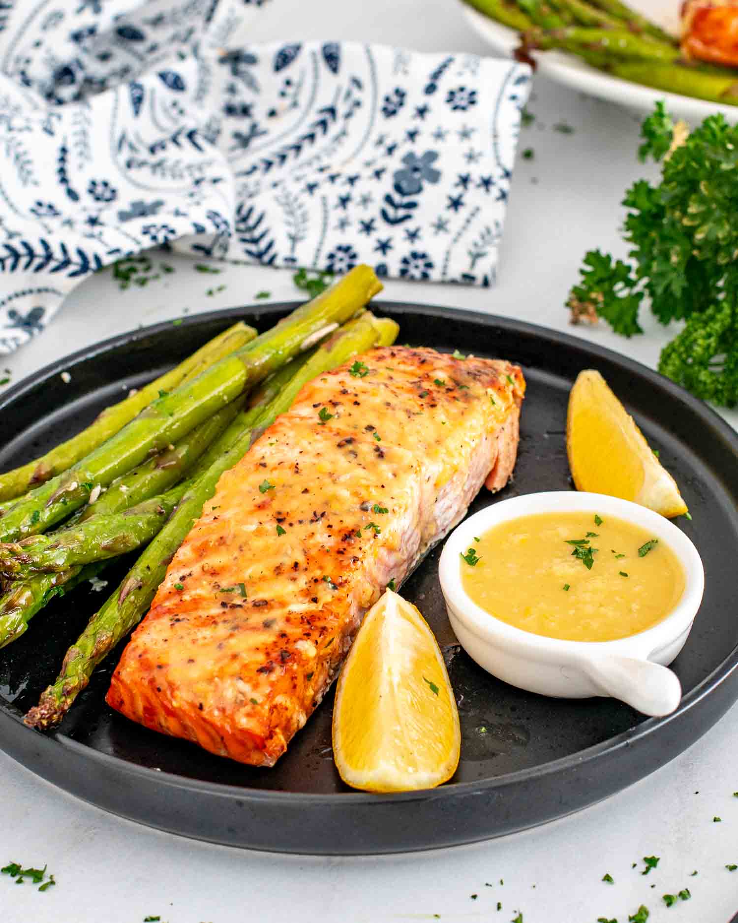 a serving of salmon and asparagus with a lemon sauce on the side.