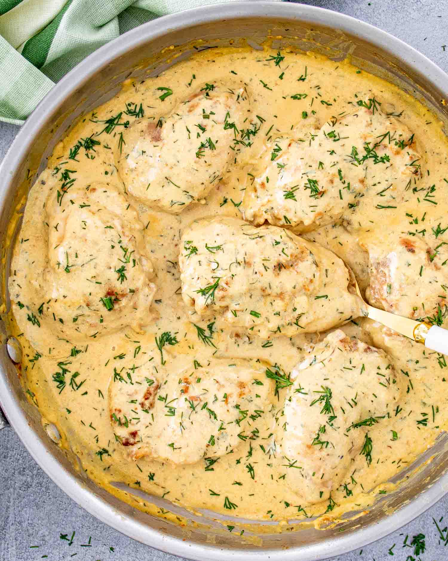 chicken thighs with creamy lemon dill sauce in a skillet with a spoon.