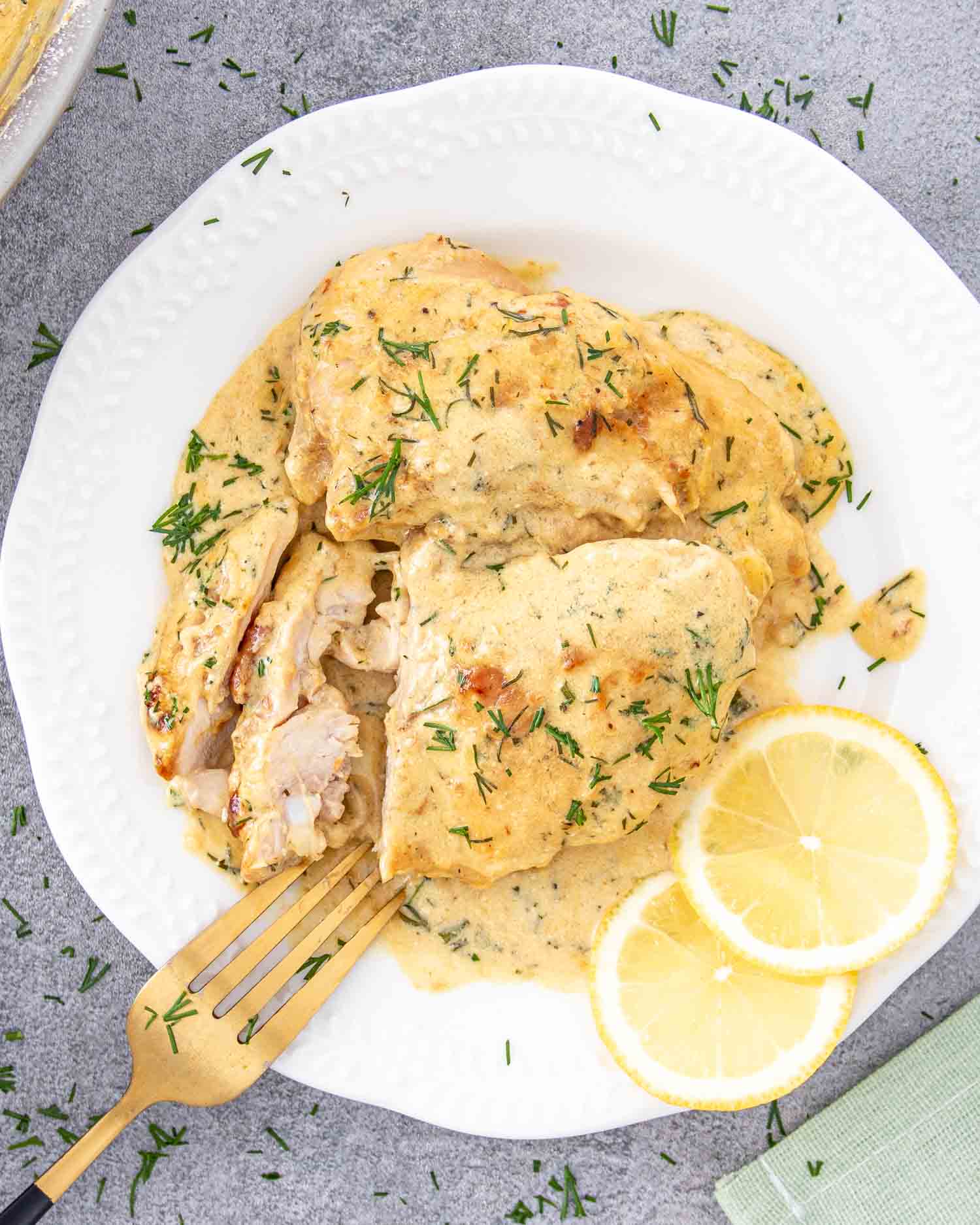 a serving of chicken thighs with creamy lemon dill sauce on a white plate.