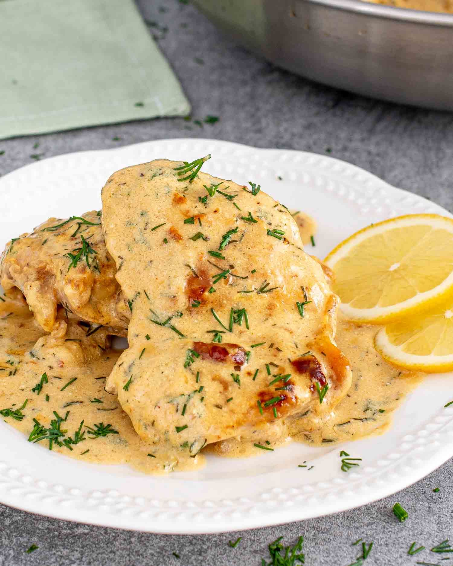 a serving of chicken thighs with creamy lemon dill sauce on a white plate.