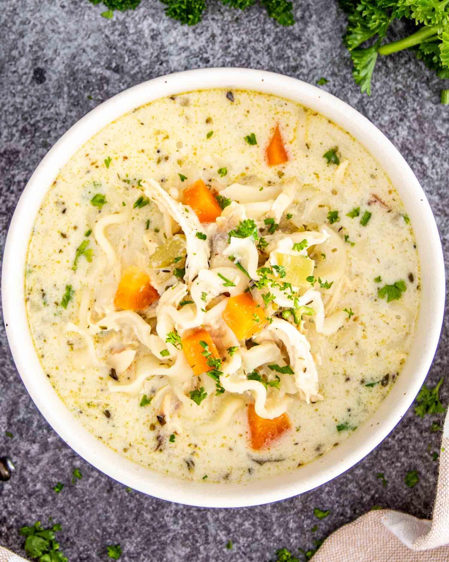 a white bowl of creamy chicken noodle soup garnished with a bit of parsley.
