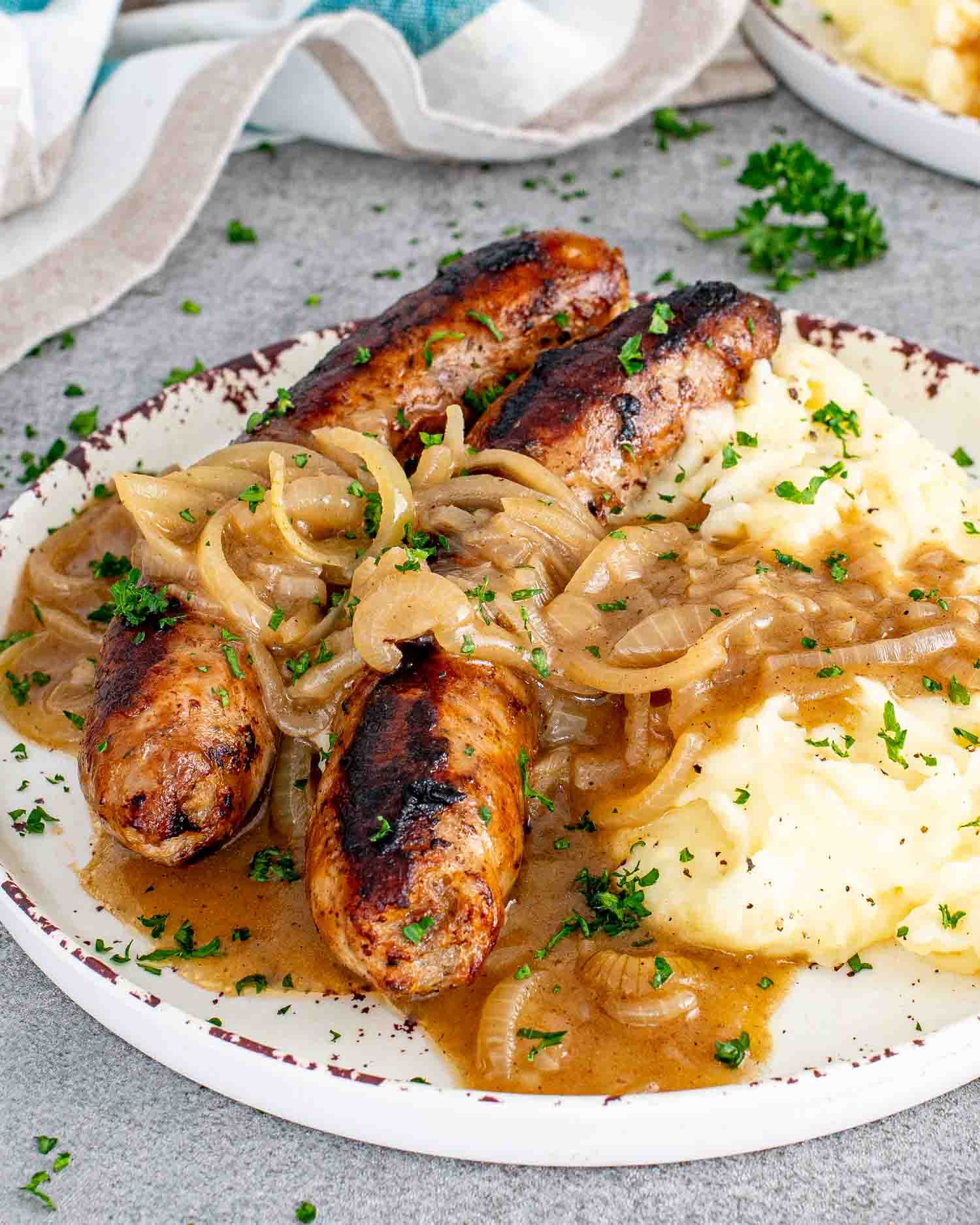 a serving of bangers and mash with onion gravy on a white plate garnished with parsley.