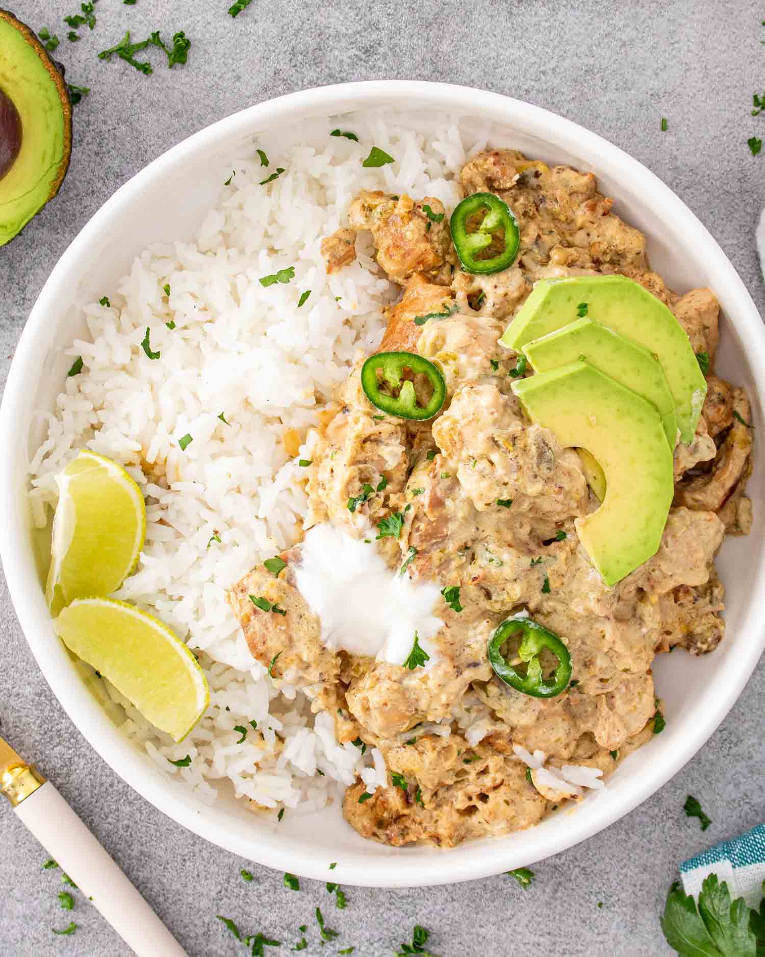 a serving of green chili chicken with rice and avocado in a white bowl.
