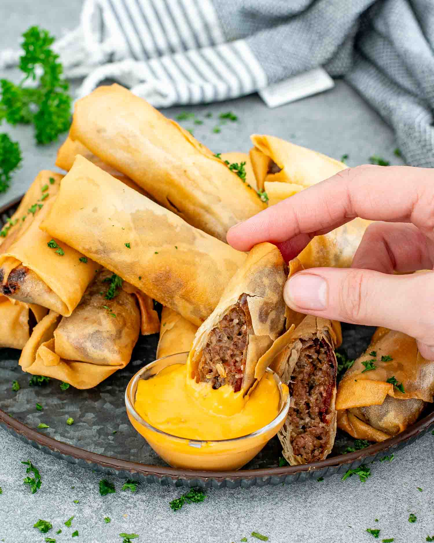 bacon cheeseburger egg rolls on a metal plate along a small bowl with cheese sauce.