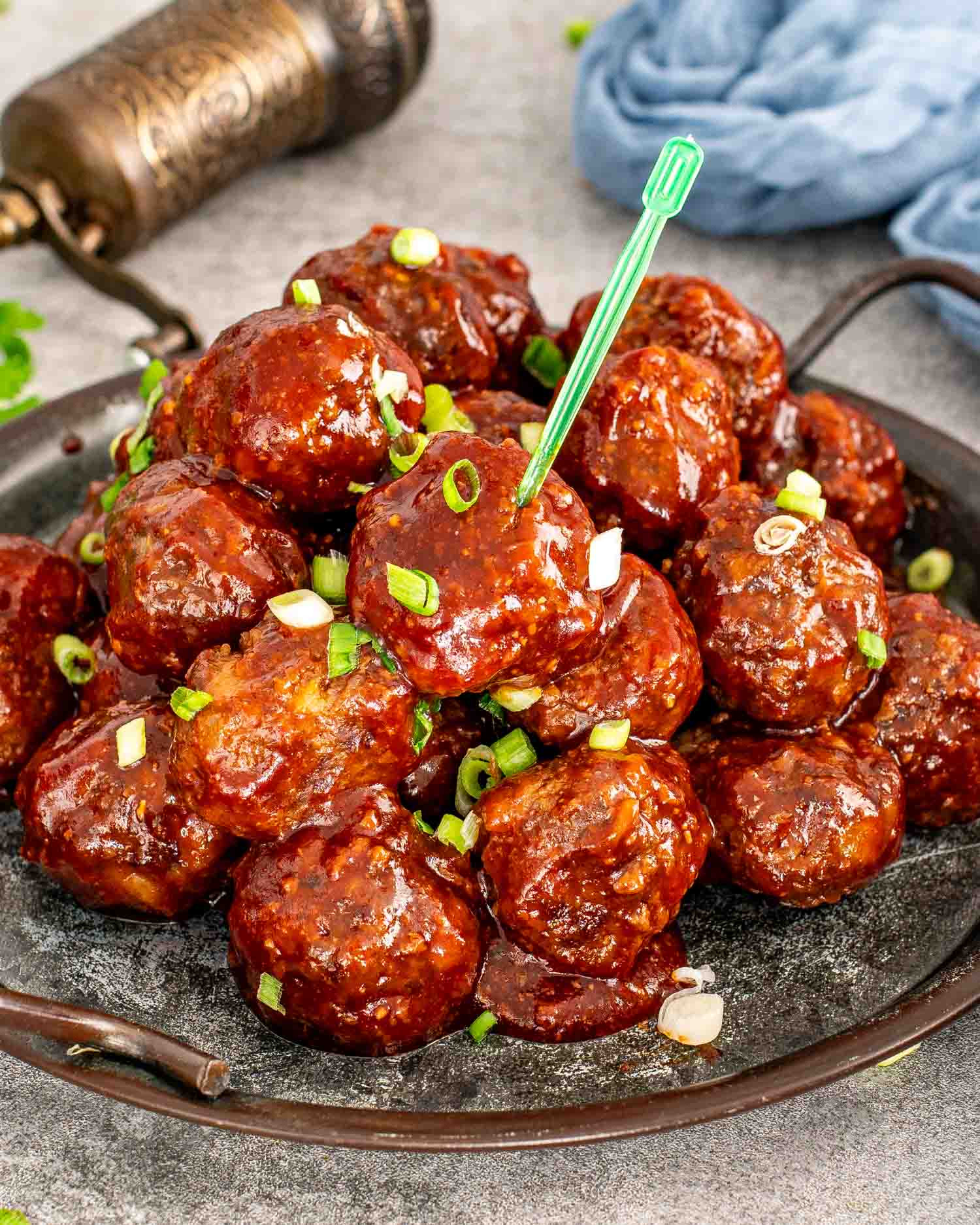 bbq meatballs in a metal plate garnished with green onions.