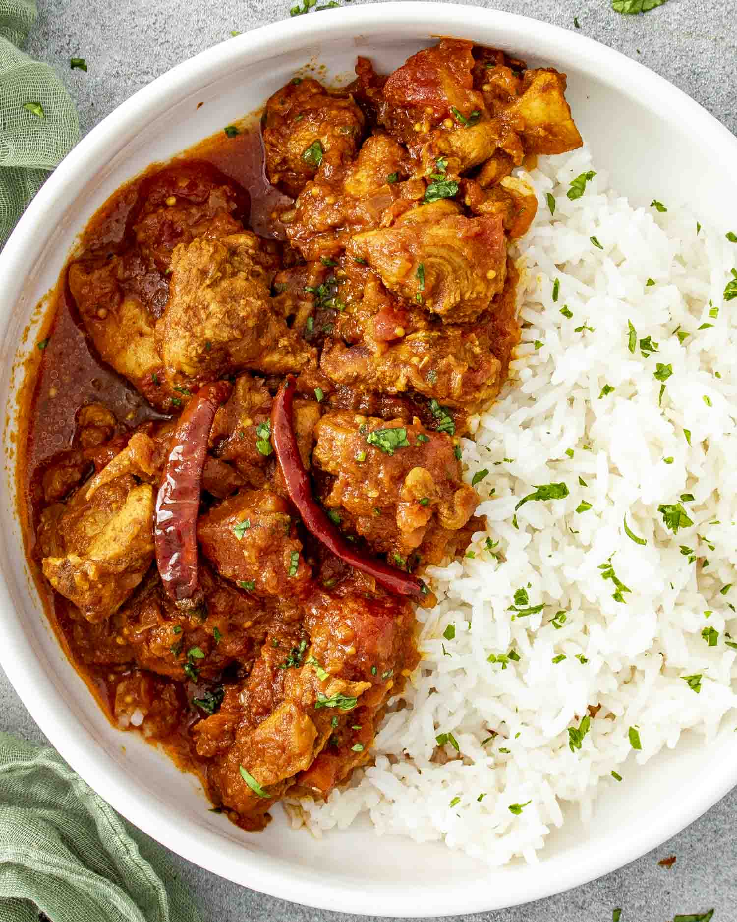 a serving of chicken vindaloo with rice in a white plate.