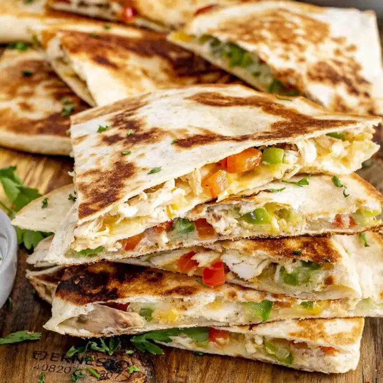 a stack of chicken quesadillas on a board with a bowl of salsa in the background.