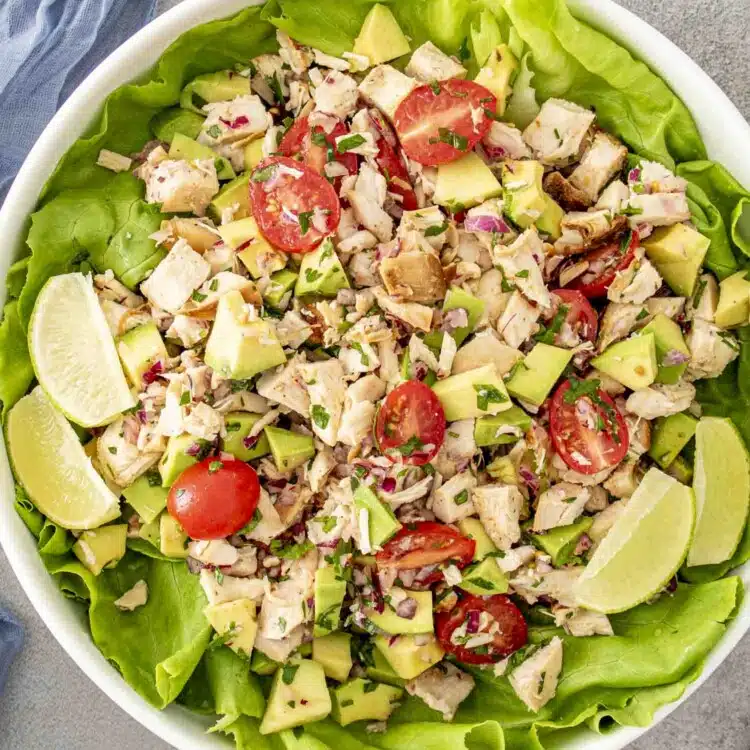 freshly made avocado chicken salad in a large white bowl on top of a bed of lettuce.