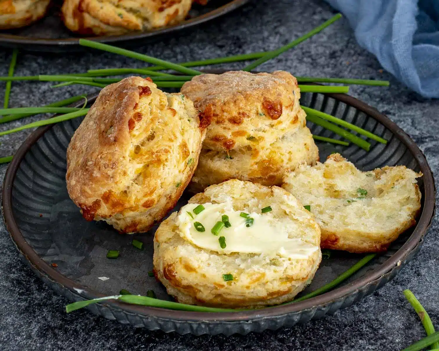 Close view of cheddar chive biscuits, one split with butter and chives on top, showing soft flaky interior.
