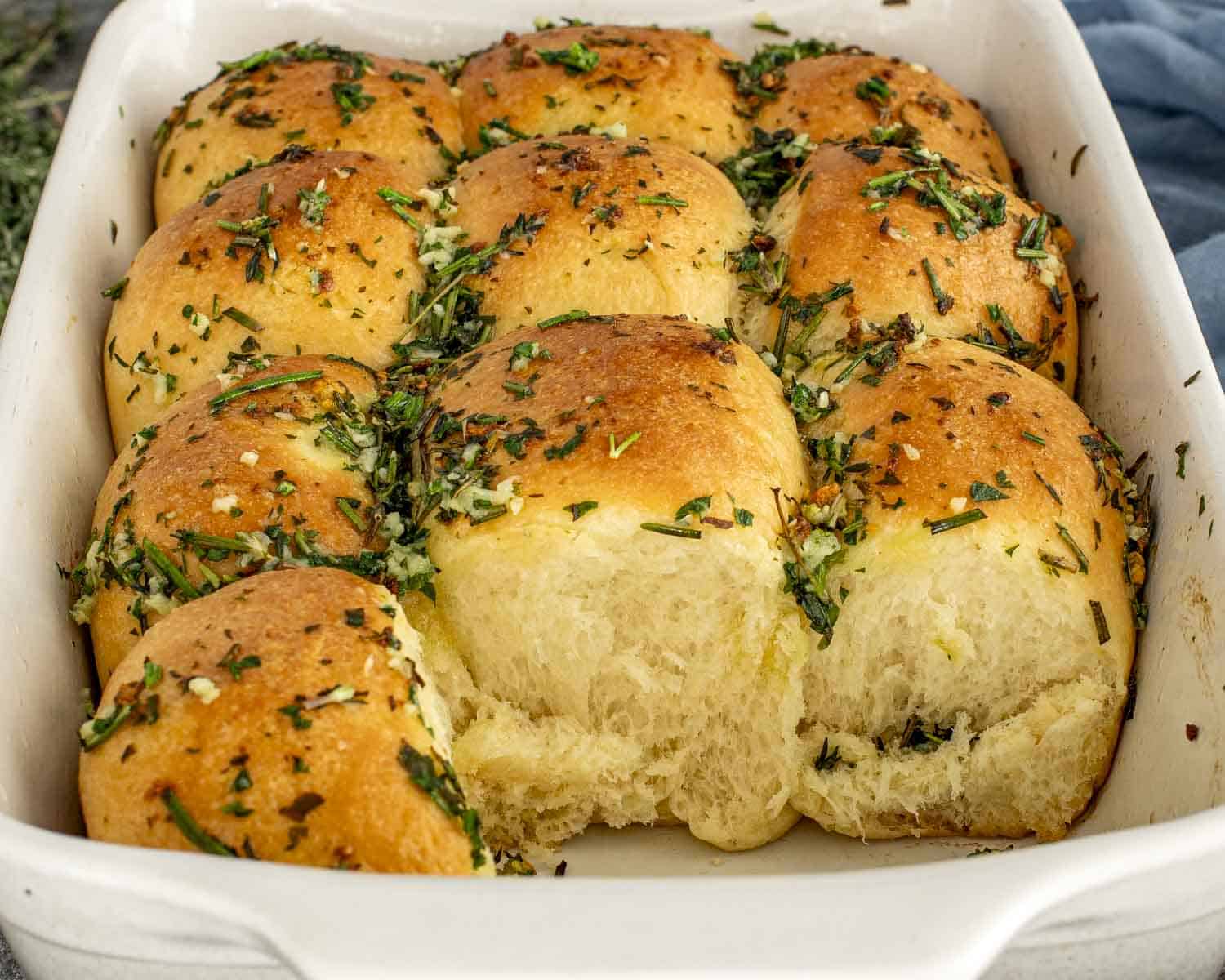 Soft, fluffy garlic herb rolls pulled apart in a baking dish, showing tender interior and buttery herb topping.