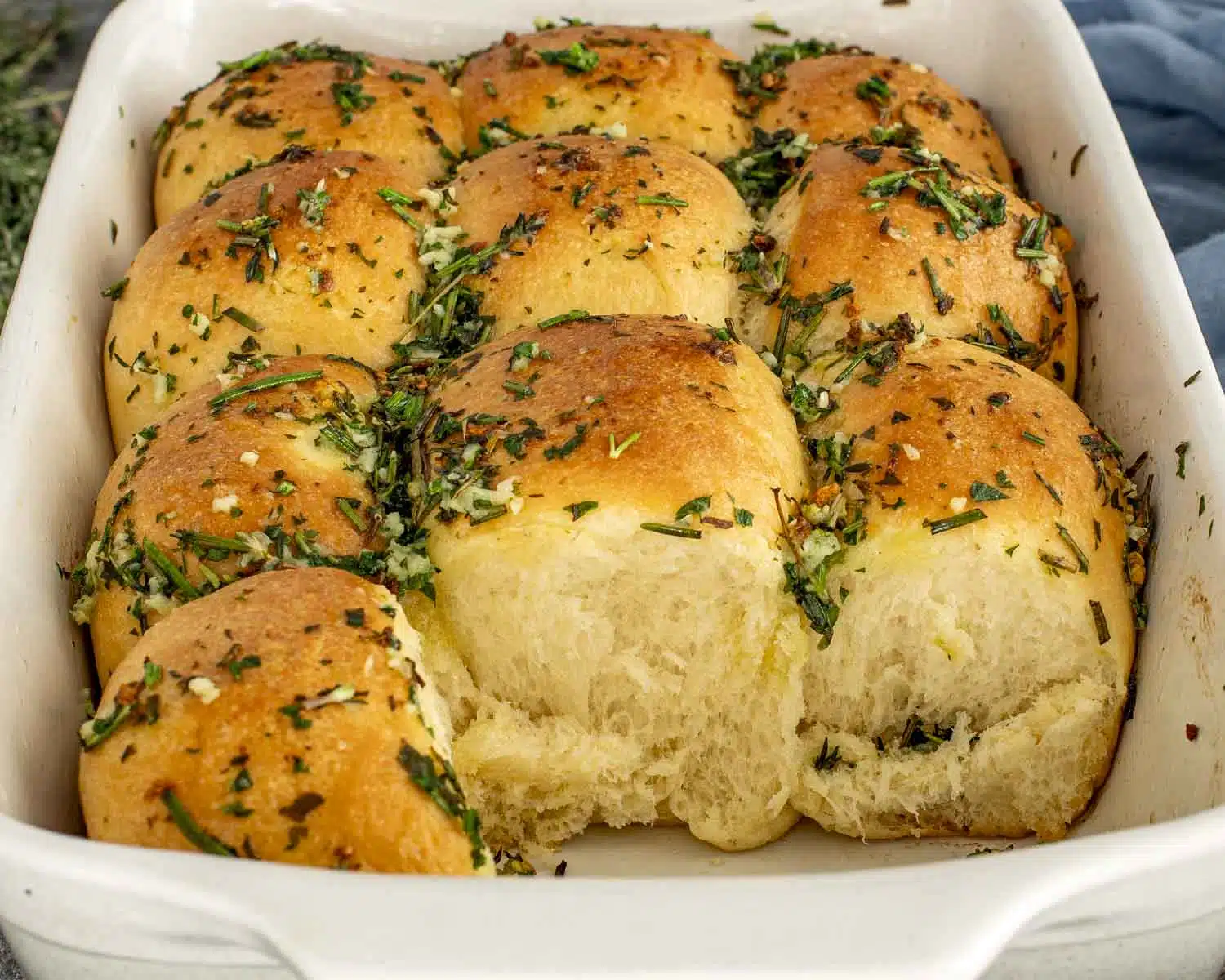 Soft, fluffy garlic herb rolls pulled apart in a baking dish, showing tender interior and buttery herb topping.