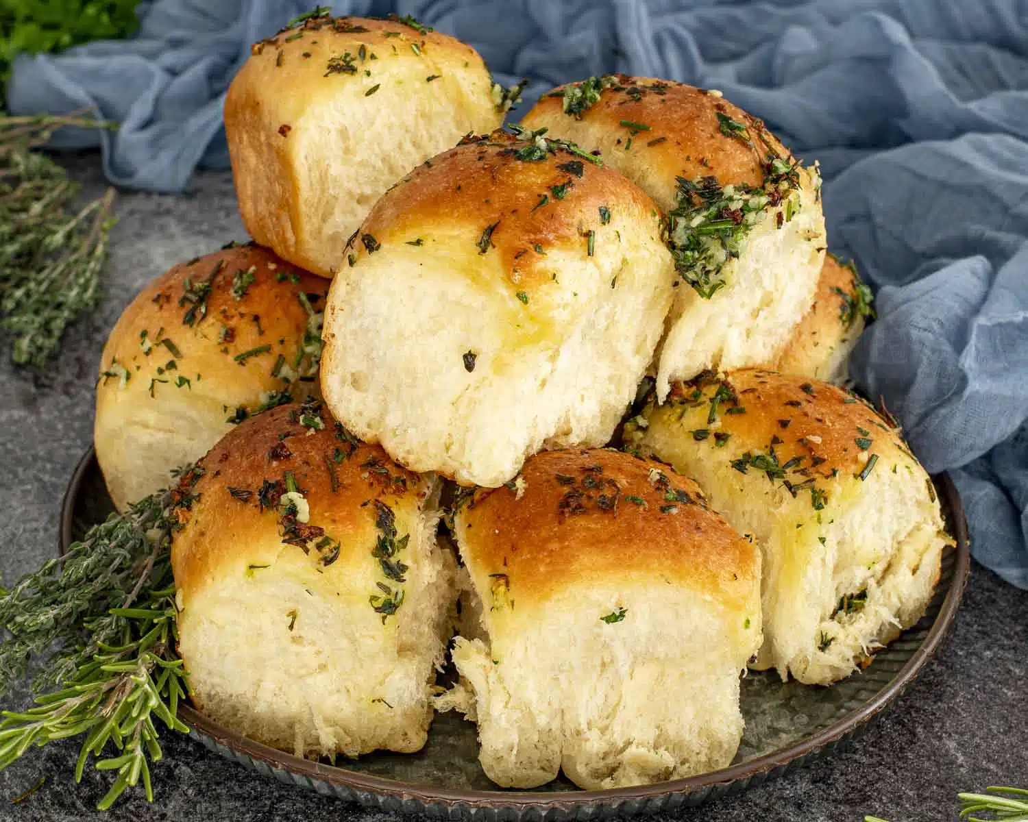 Close-up of garlic herb pull apart rolls stacked high, highlighting golden crust, soft interior, and generous herb butter.