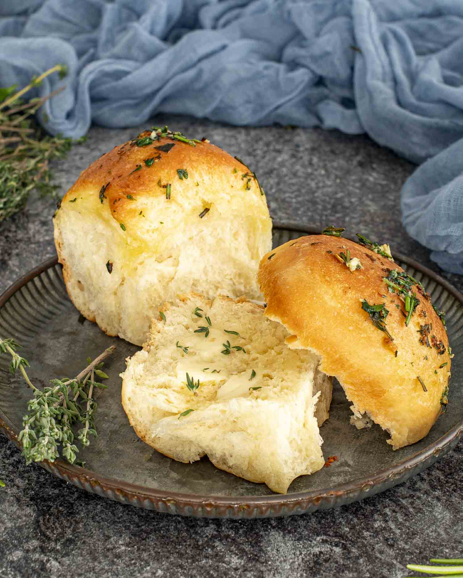Warm garlic herb roll split open on a plate, showing soft fluffy texture with melted butter and fresh thyme on top.