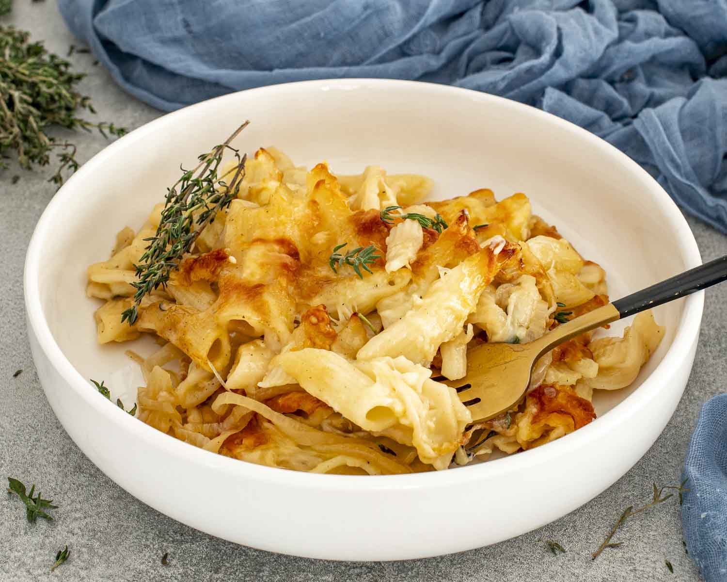 Warm French onion pasta bake scooped into a white bowl, topped with golden cheese and fresh thyme, ready to eat.