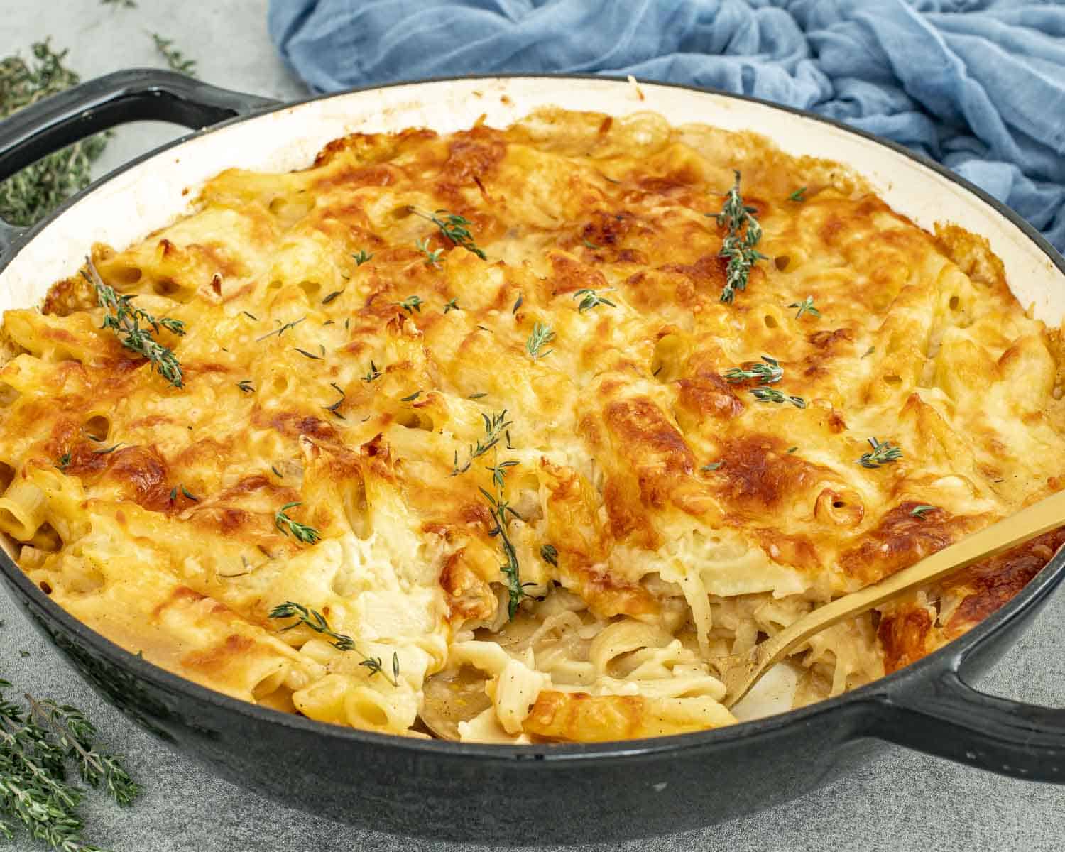 Cheesy French onion pasta bake in a cast-iron skillet, topped with browned bubbly cheese and scattered fresh thyme sprigs.