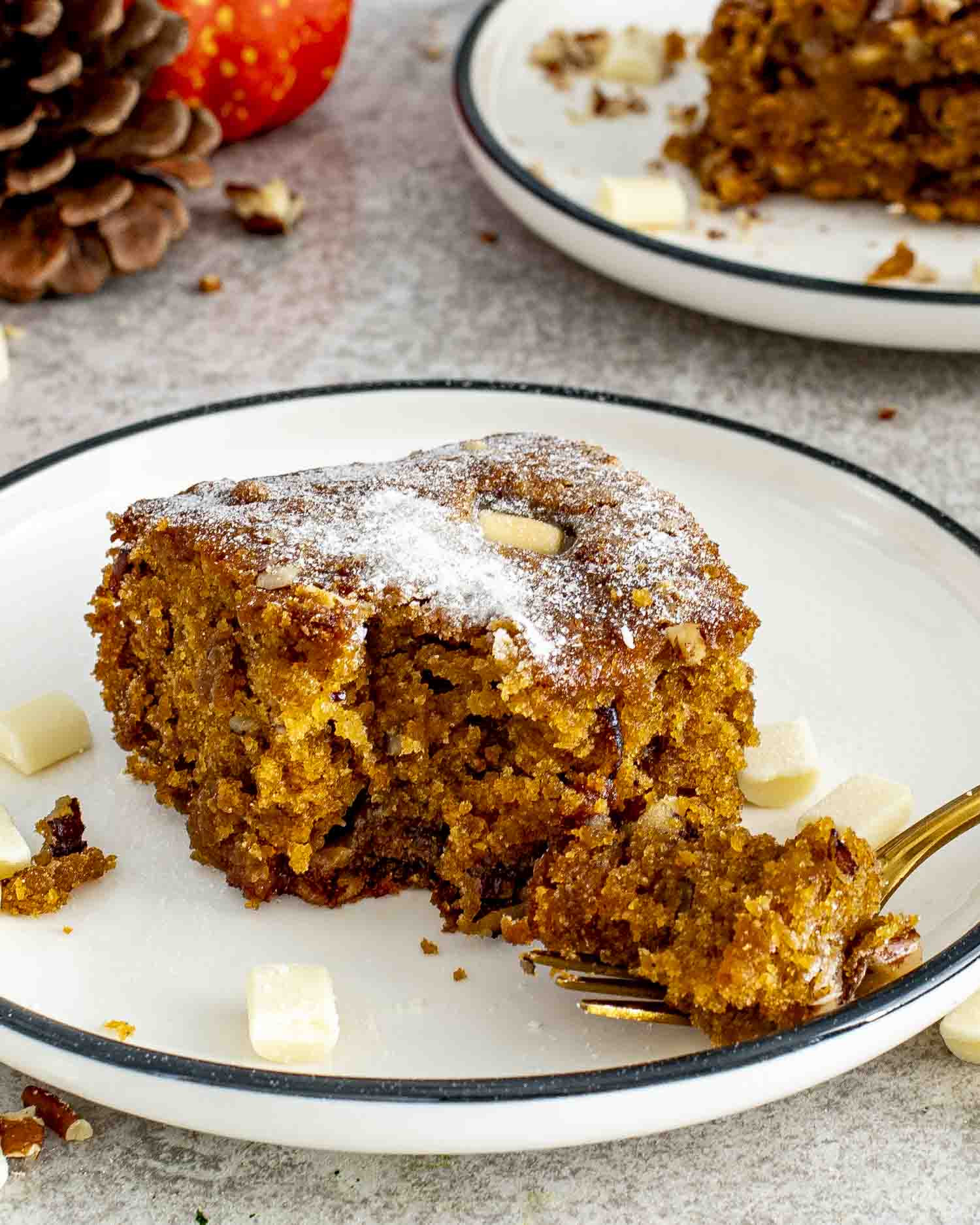Slice of pumpkin spice blondie on a plate, soft and chewy with white chocolate pieces and a dusting of powdered sugar.