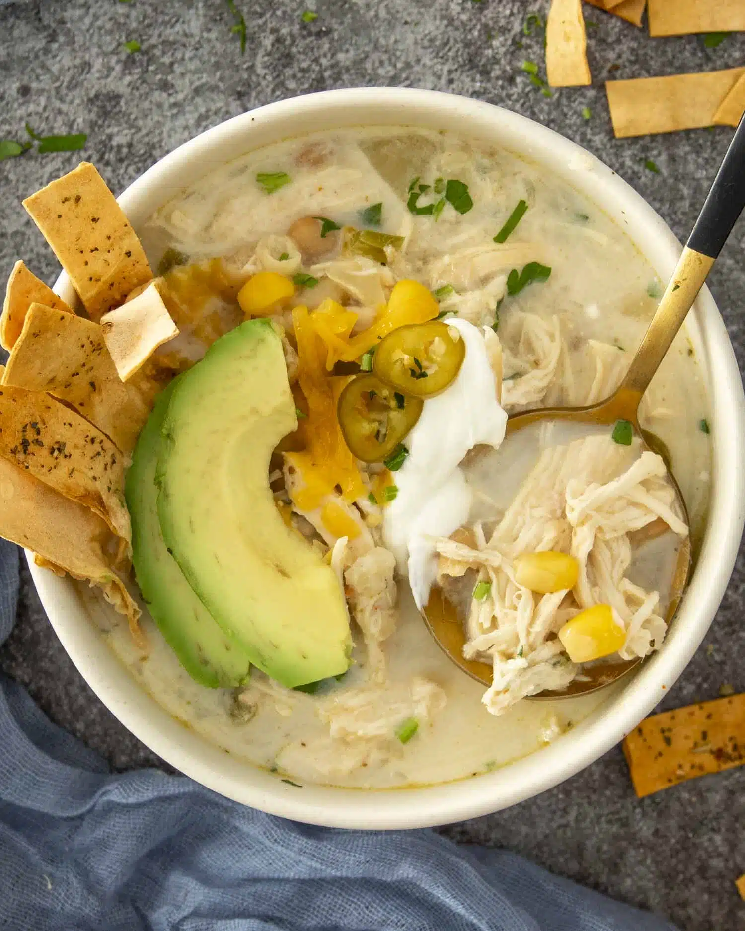Bowl of white chicken chili topped with avocado, cheese, sour cream and tortilla strips for a hearty, flavorful presentation.