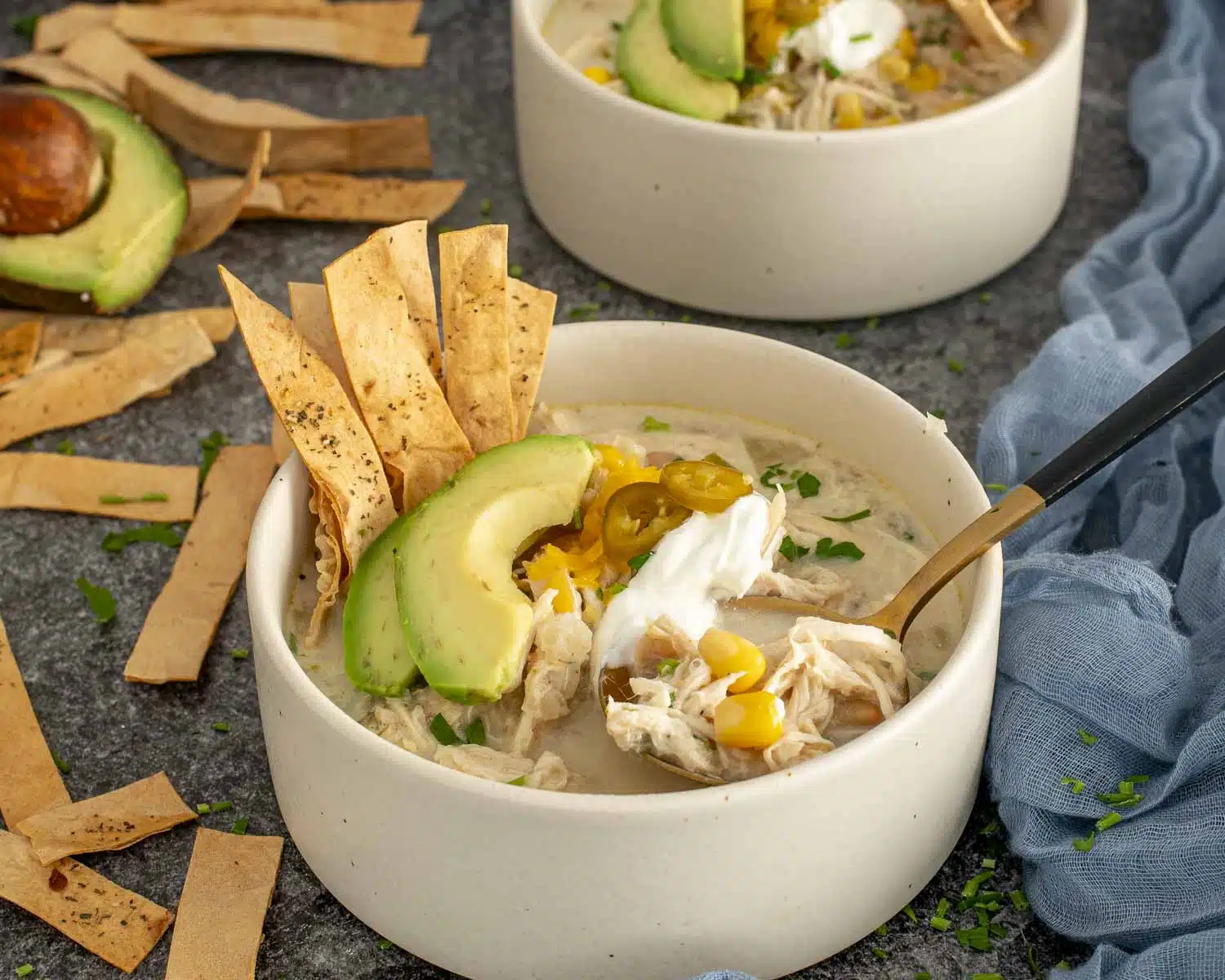 Two bowls of creamy white chicken chili topped with avocado, jalape&ntilde;os, cheese and tortilla strips for a cozy meal.Two bowls of creamy white chicken chili topped with avocado, jalape&ntilde;os, cheese and tortilla strips for a cozy meal.