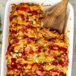 Spoon serving BBQ chicken casserole showing cheesy penne pasta, shredded chicken, bacon bits, green onions, and barbecue sauce.