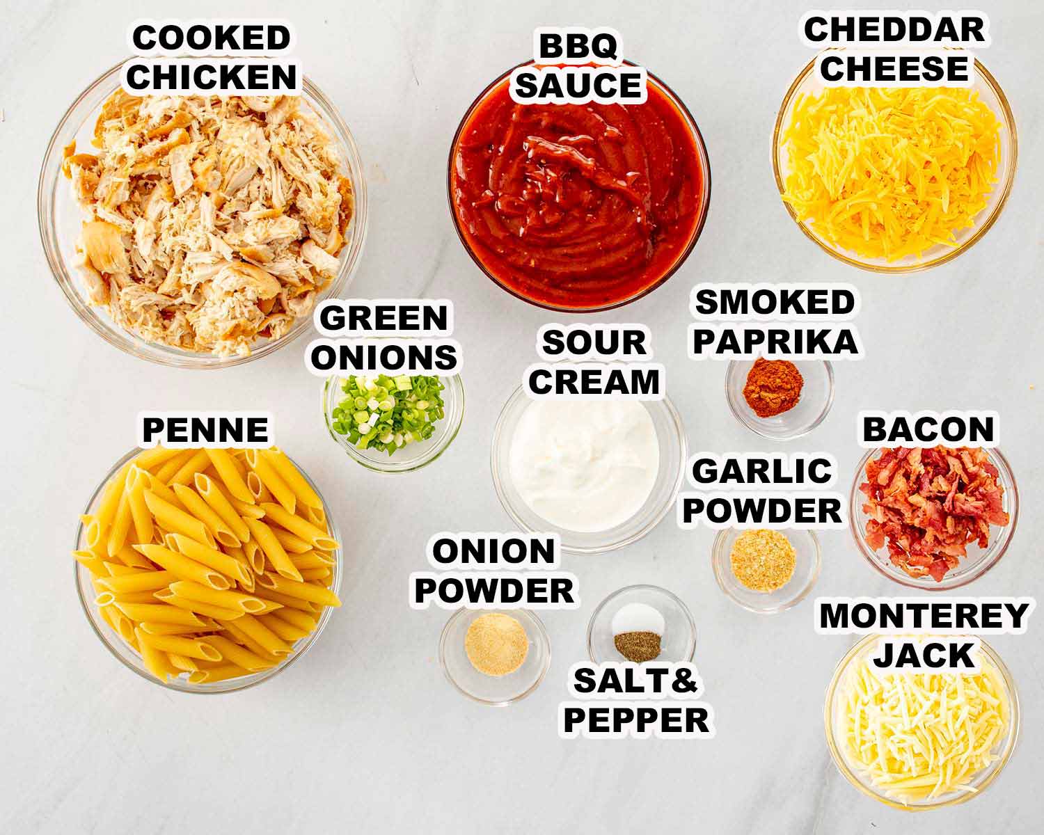 Ingredients for BBQ chicken casserole including cooked chicken, penne pasta, BBQ sauce, sour cream, cheddar, Monterey Jack, bacon, and seasonings.