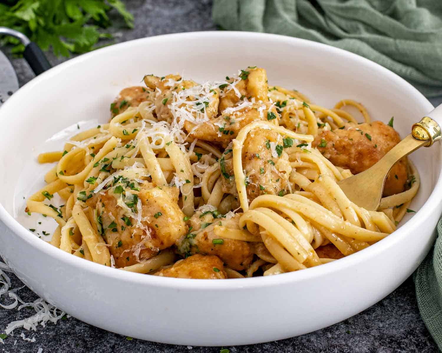 Serving bowl of chicken scampi with linguine, juicy chicken, garlic butter sauce, Parmesan cheese, and fresh parsley.