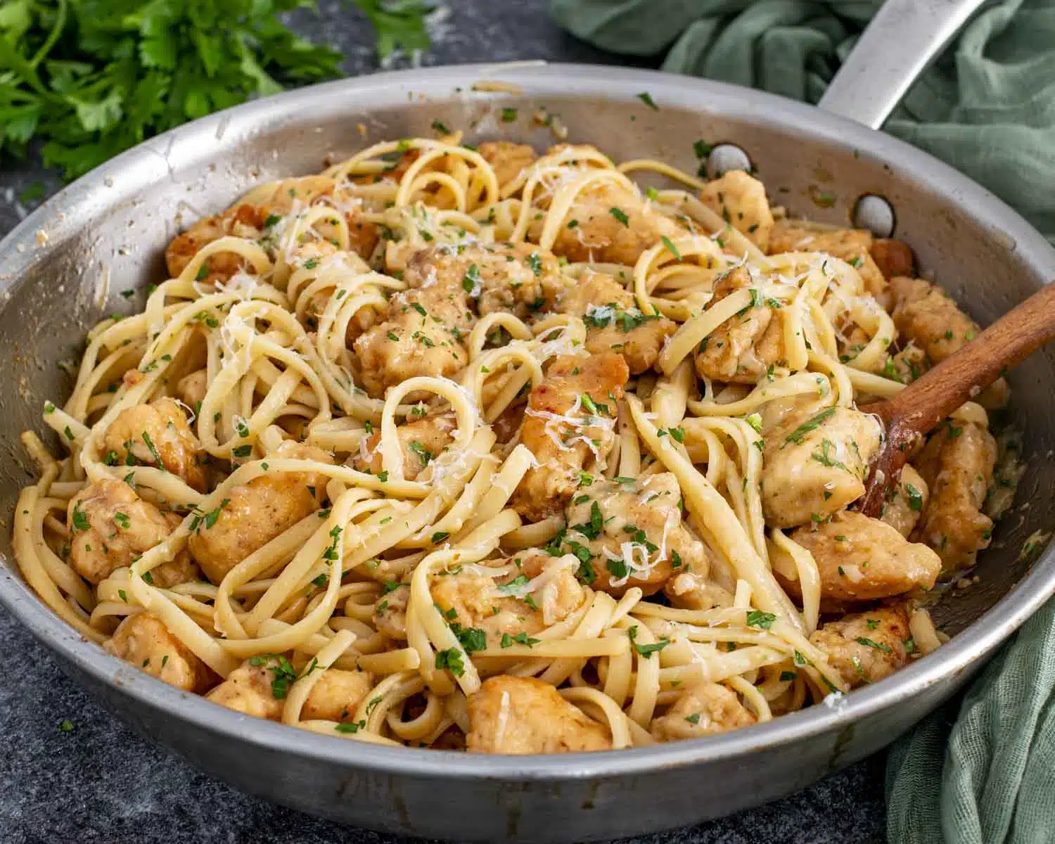 Close-up of chicken scampi pasta in skillet showing tender chicken, glossy sauce, fresh parsley, and grated Parmesan.