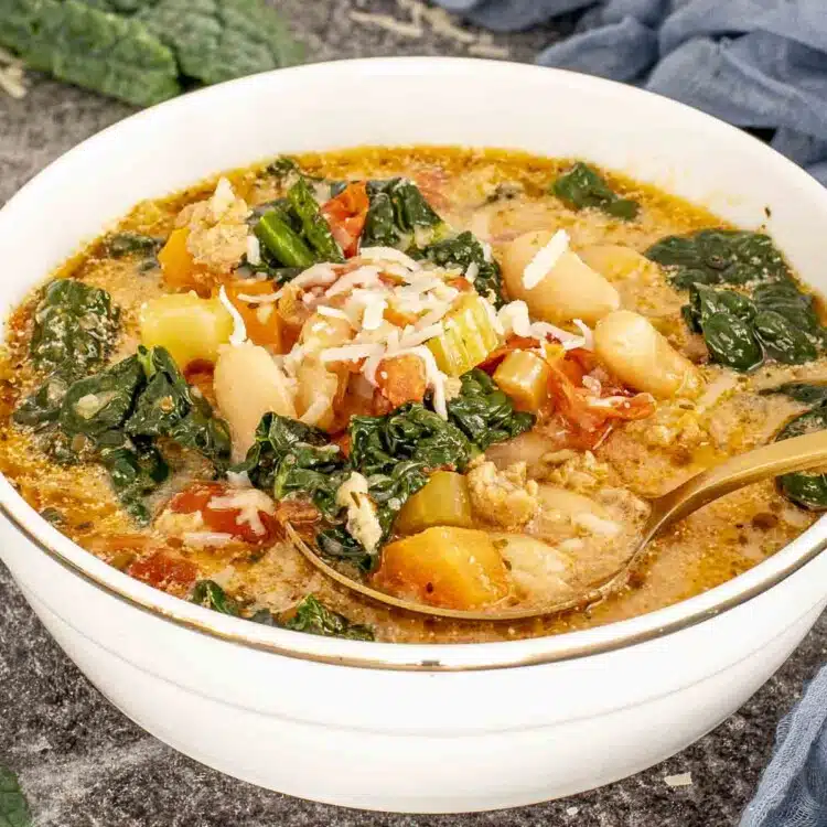 Close-up of sausage and white bean soup served in a bowl with Parmesan, kale, beans, tomatoes, and sausage.