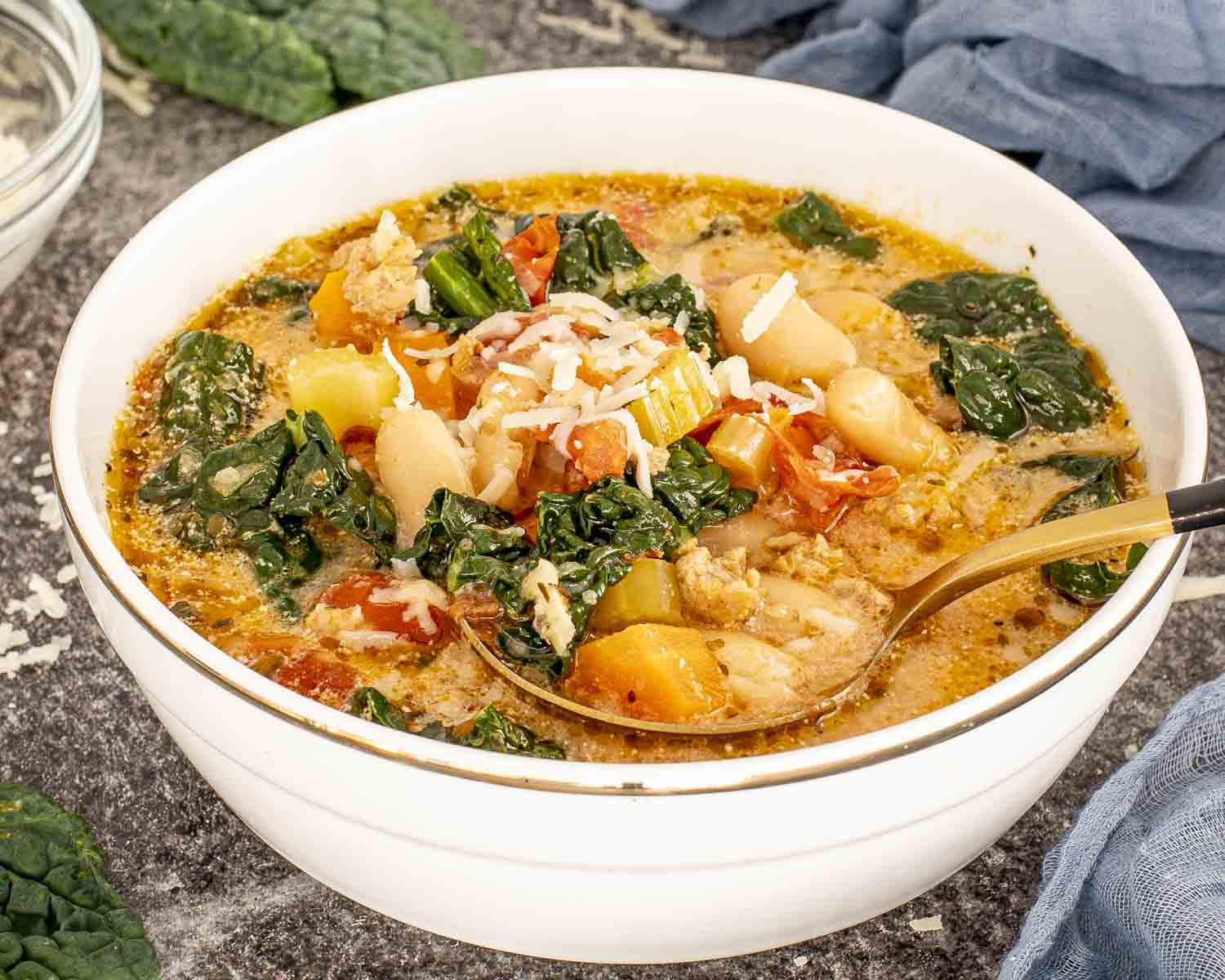 Close-up of sausage and white bean soup served in a bowl with Parmesan, kale, beans, tomatoes, and sausage.