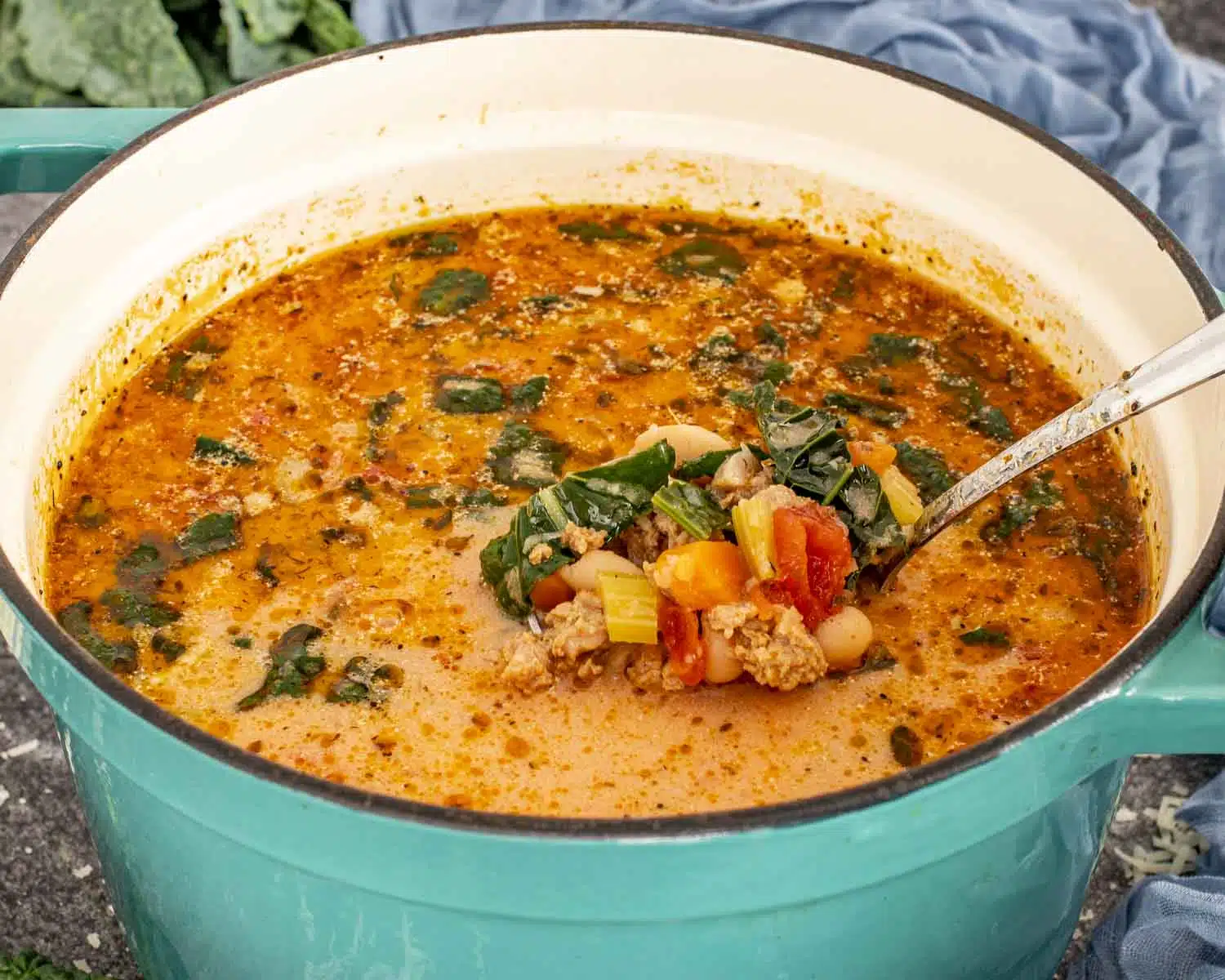 Creamy sausage and white bean soup cooked in a Dutch oven with kale, beans, vegetables, and rich seasoned broth.