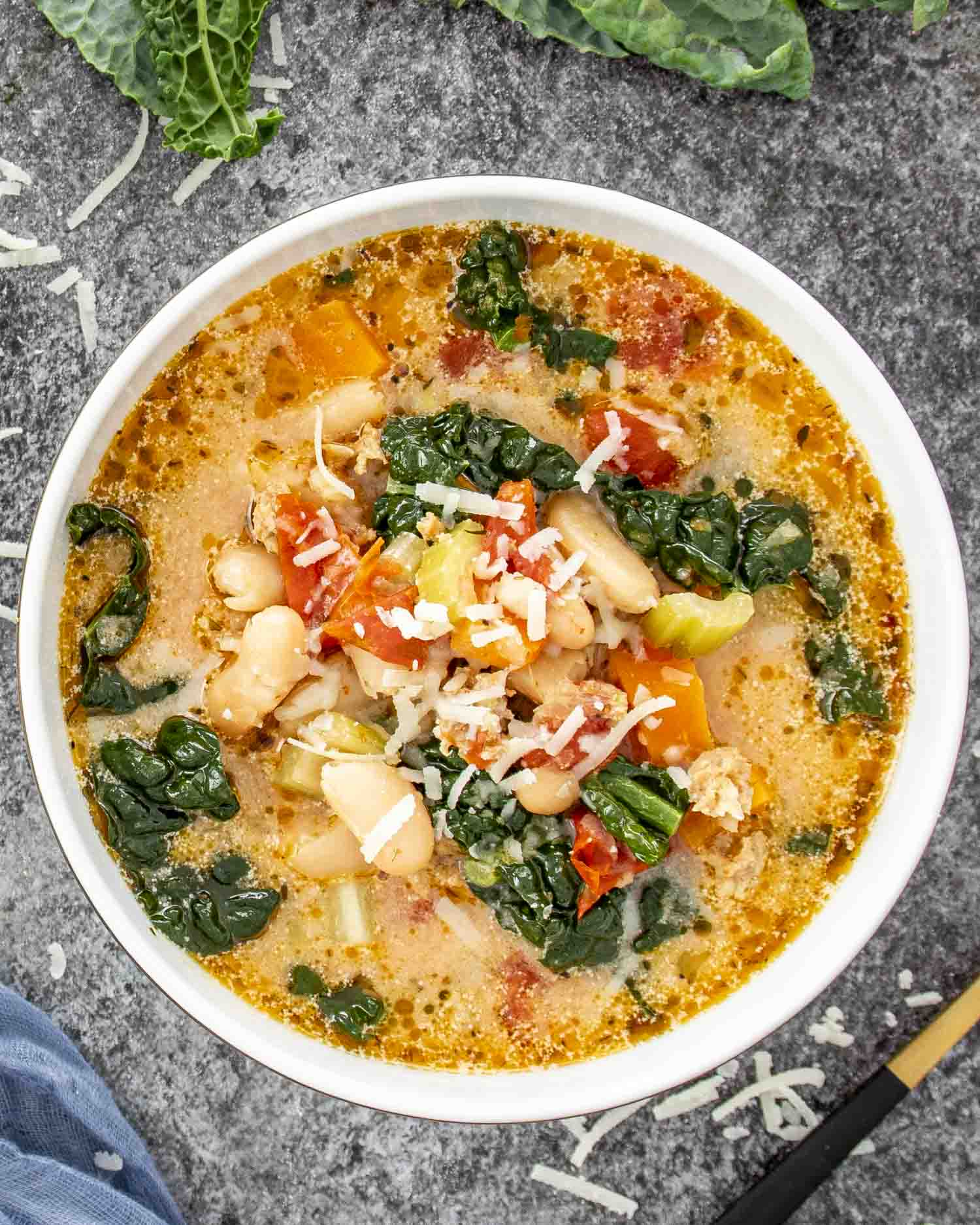 Bowl of sausage and white bean soup topped with Parmesan, featuring cannellini beans, kale, tomatoes, and creamy broth.