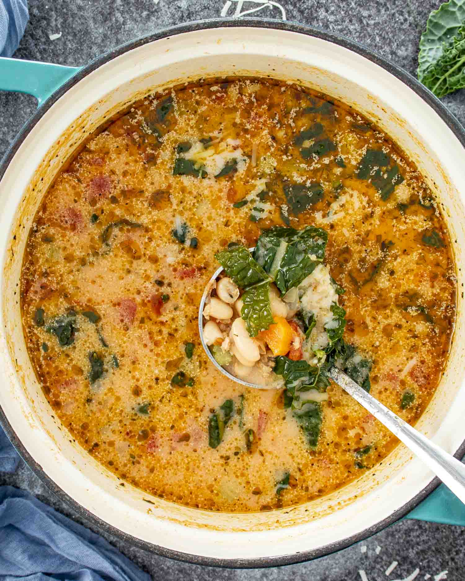 Sausage and white bean soup simmering in a Dutch oven with creamy broth, kale, beans, vegetables, and Italian sausage.