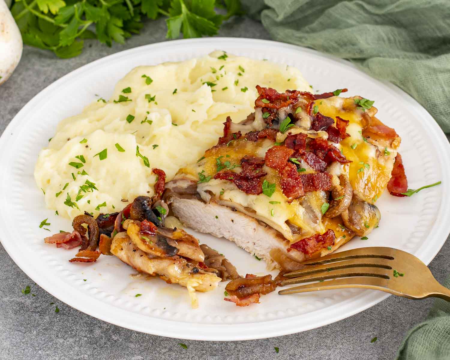 Sliced smothered chicken breast showing juicy interior topped with mushrooms, onions, bacon, and melted cheese.