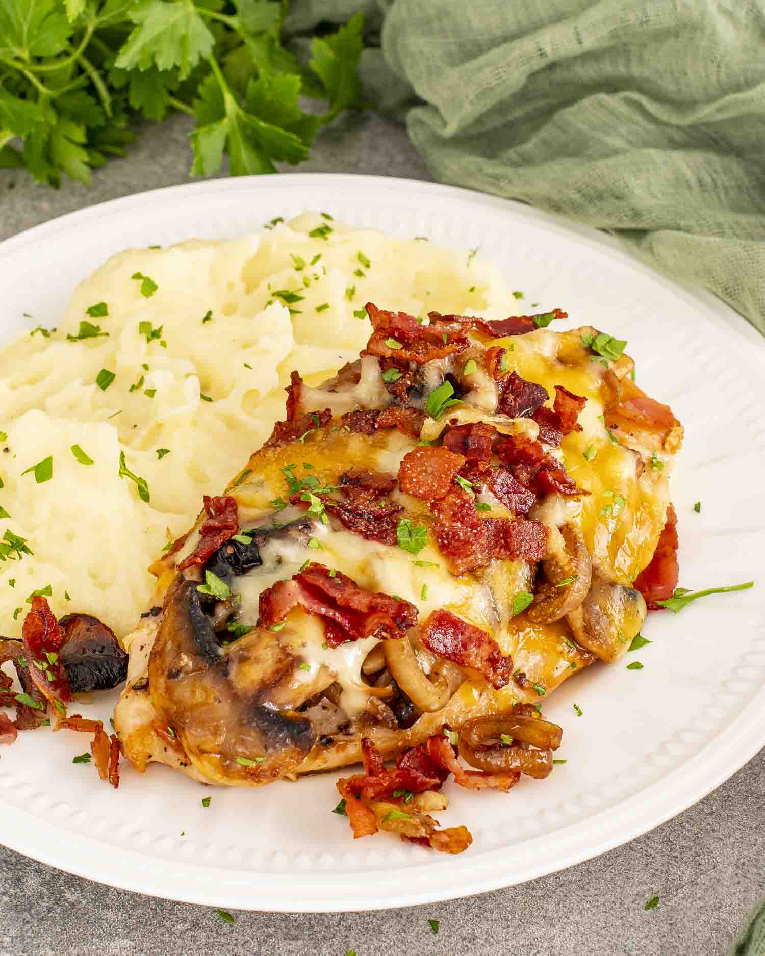 Copycat Texas Roadhouse smothered chicken served hot with mushrooms, onions, melted cheese, and bacon on a white plate.