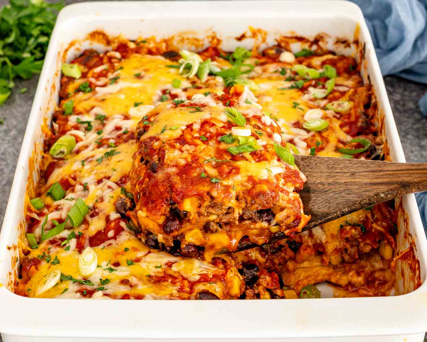 Baked beef enchilada casserole in a white dish topped with melted cheese, green onions, and fresh cilantro.