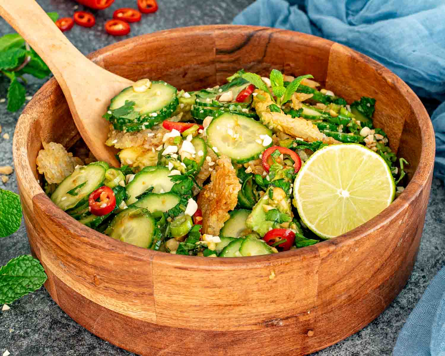 Close up of crispy rice cucumber salad with sesame seeds, chili slices, fresh herbs, and lime wedge on the side.