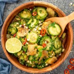 Crispy rice cucumber salad with sliced cucumbers, herbs, chili, peanuts, and golden rice shards in a wooden bowl.