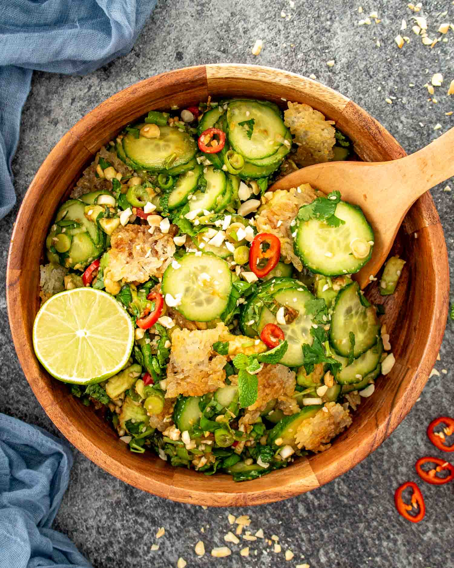 Crispy rice cucumber salad with sliced cucumbers, herbs, chili, peanuts, and golden rice shards in a wooden bowl.