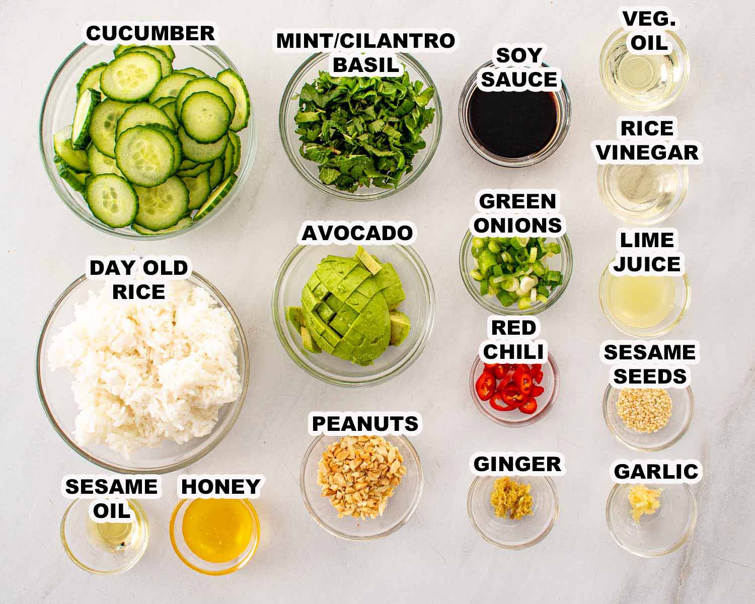 Day old rice, cucumbers, avocado, fresh herbs, peanuts, chili, and sesame dressing ingredients arranged on a light surface.