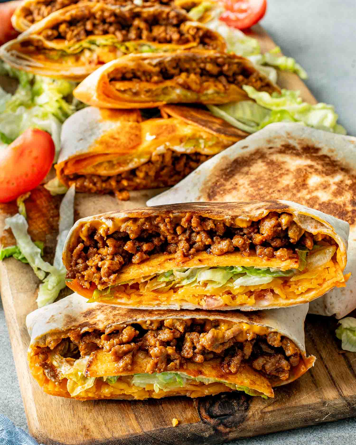 Stacked Taco Bell Crunchwrap Supreme copycat wraps on a wooden board with visible crunchy tostada and seasoned beef layers.