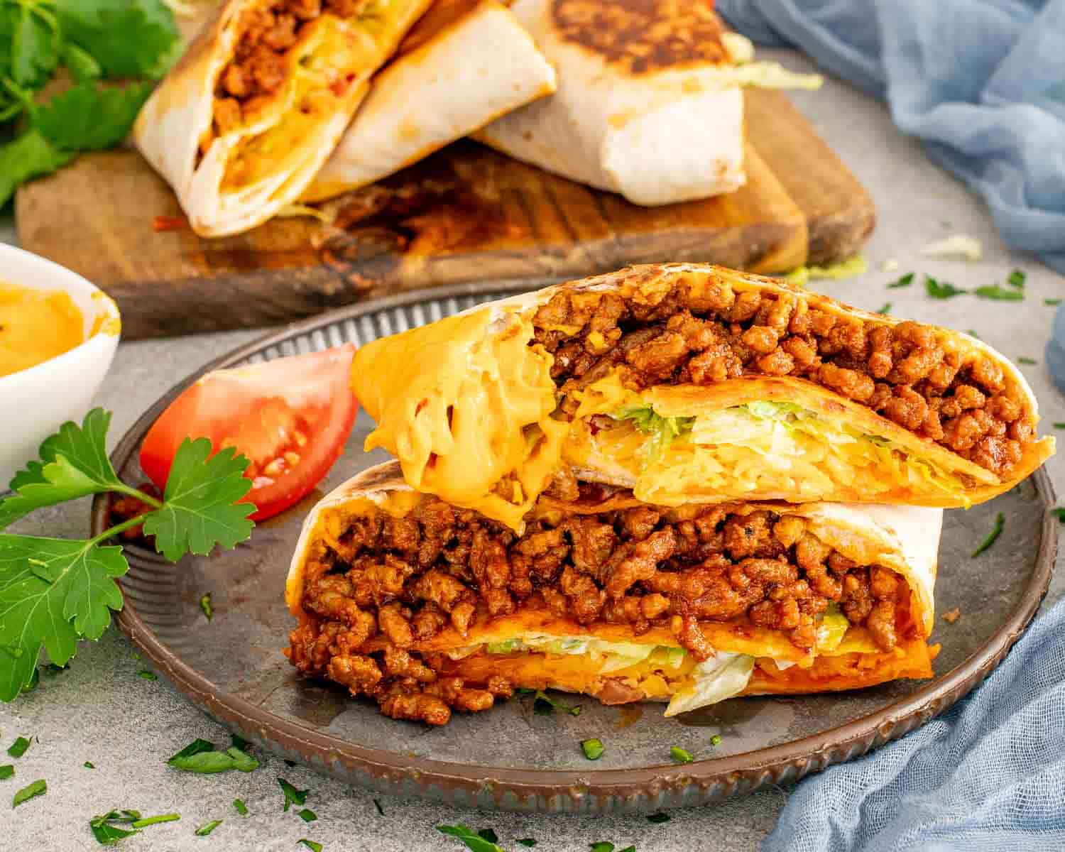 Halved Taco Bell Crunchwrap Supreme copycat showing layers of seasoned ground beef, nacho cheese, lettuce, and crunchy tostada shell.
