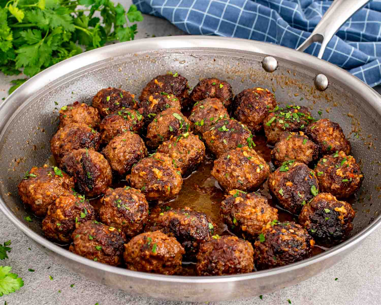 Skillet filled with browned meatballs coated in buttery garlic lemon sauce with herbs and red pepper flakes.
