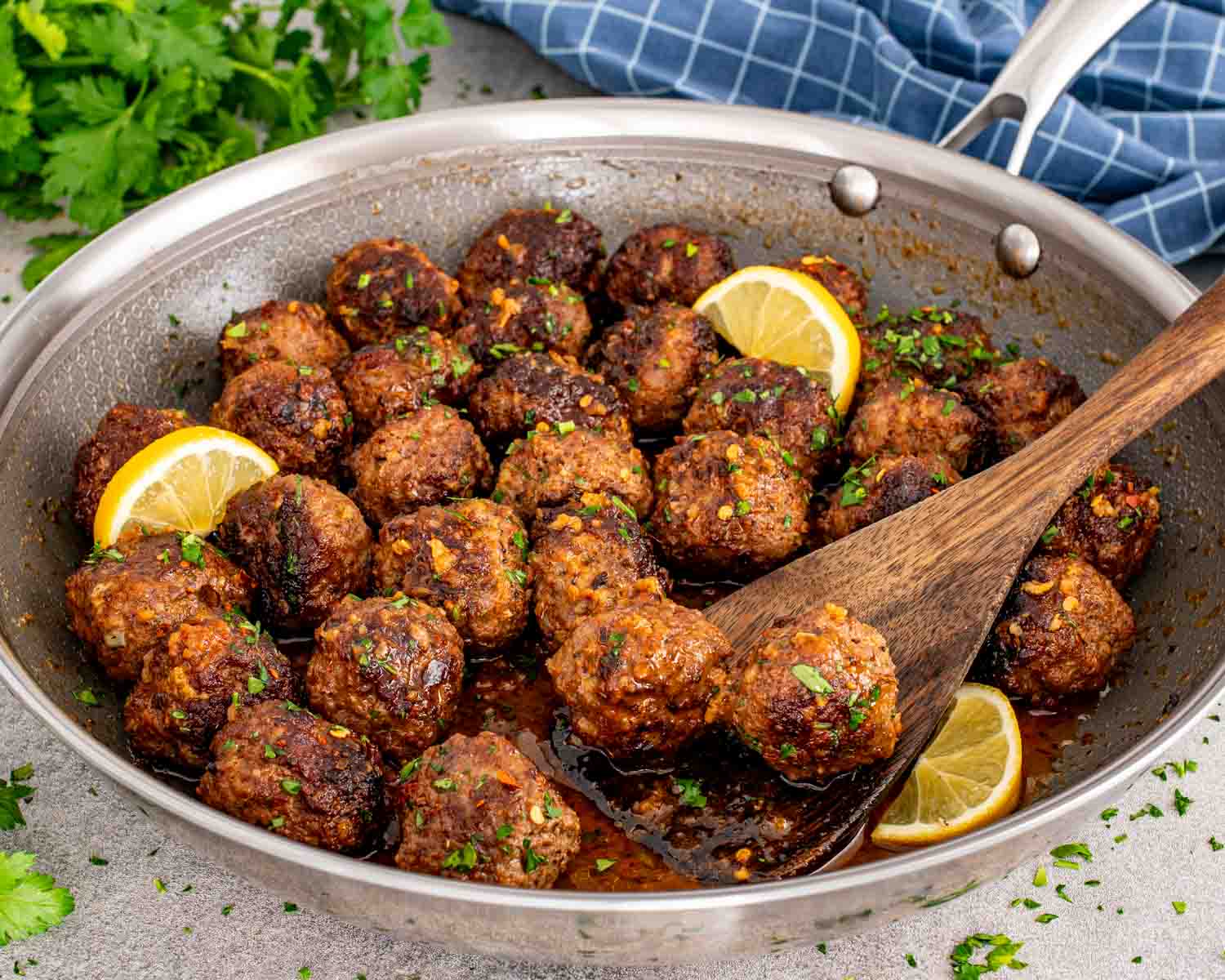 Skillet filled with browned meatballs coated in buttery garlic lemon sauce with herbs and red pepper flakes.
