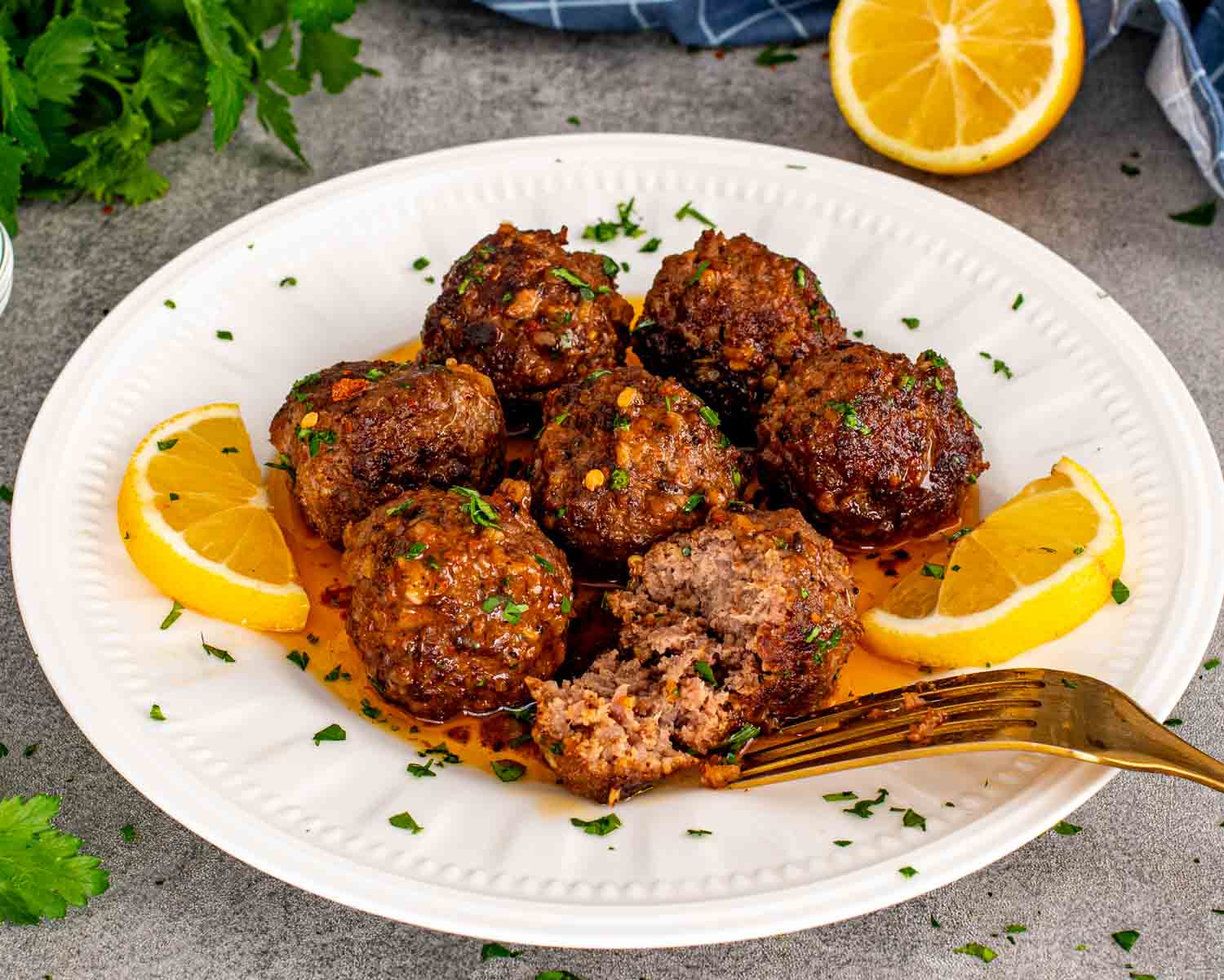 Close up of cowboy butter meatballs with one cut open showing juicy interior, served with lemon wedges and herb butter sauce.