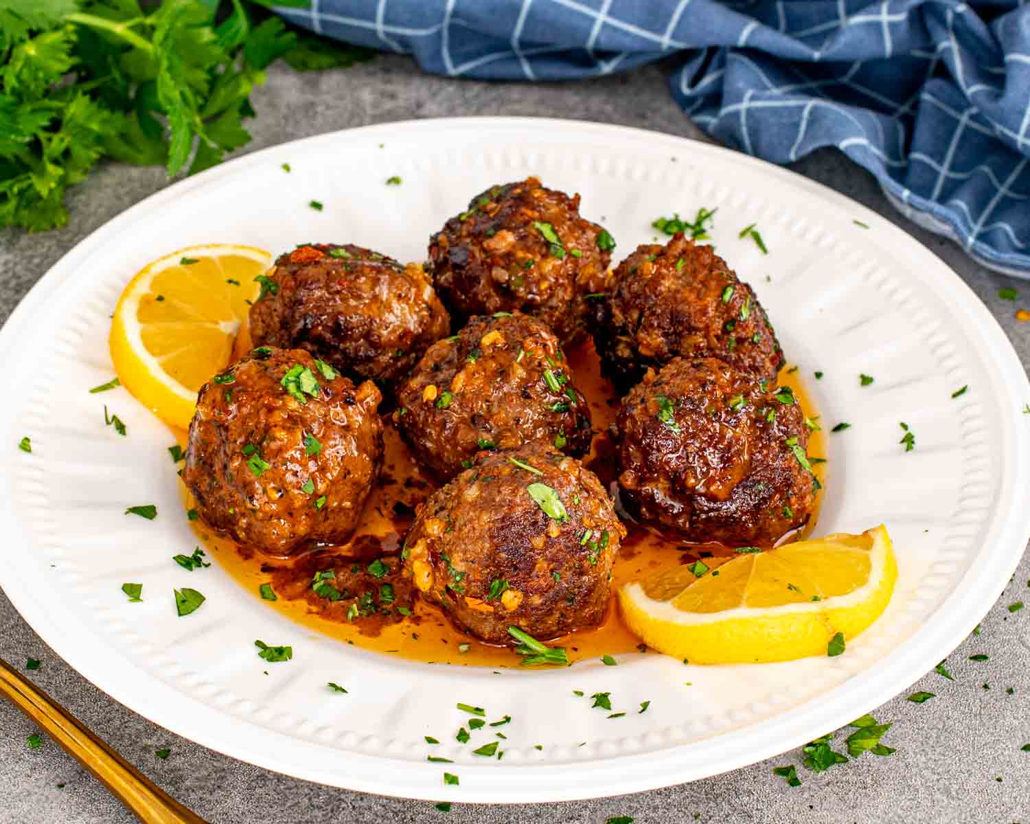 Cowboy butter meatballs served on a white plate with lemon wedges, parsley, and rich buttery sauce drizzled over.