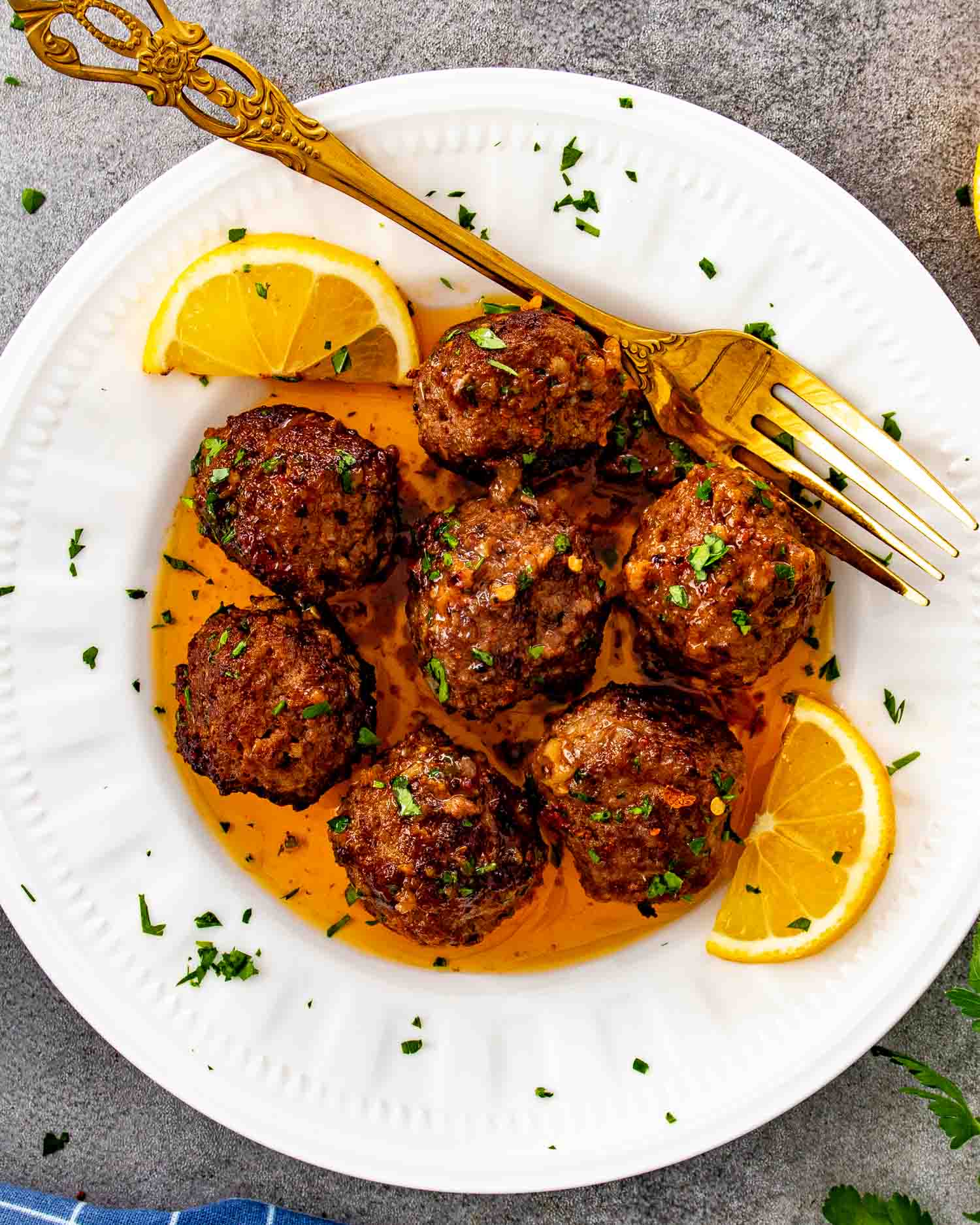 Cowboy butter meatballs served on a white plate with lemon wedges, parsley, and rich buttery sauce drizzled over.