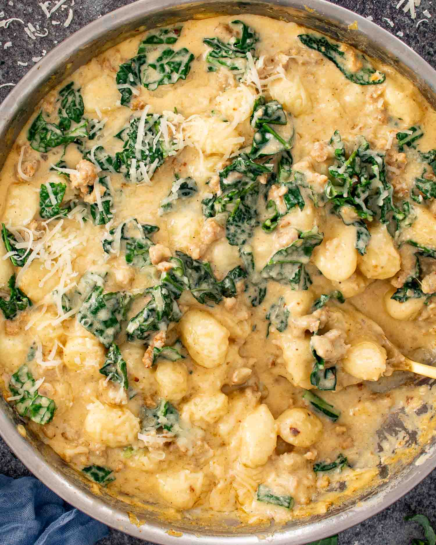 Skillet gnocchi with sausage and kale simmering in a creamy Parmesan sauce in a large pan.
