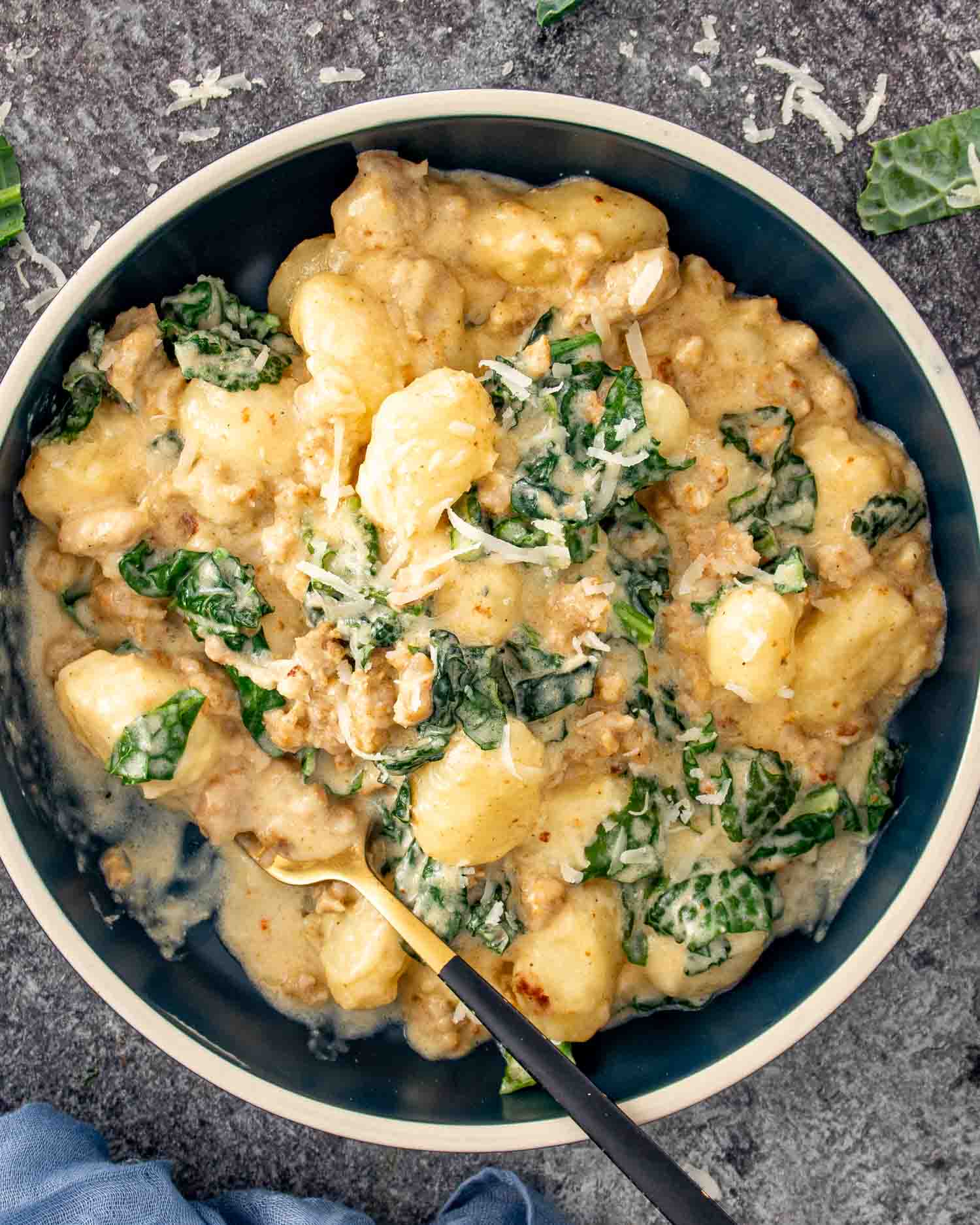 Creamy skillet gnocchi with Italian sausage and kale served in a bowl and finished with grated Parmesan.