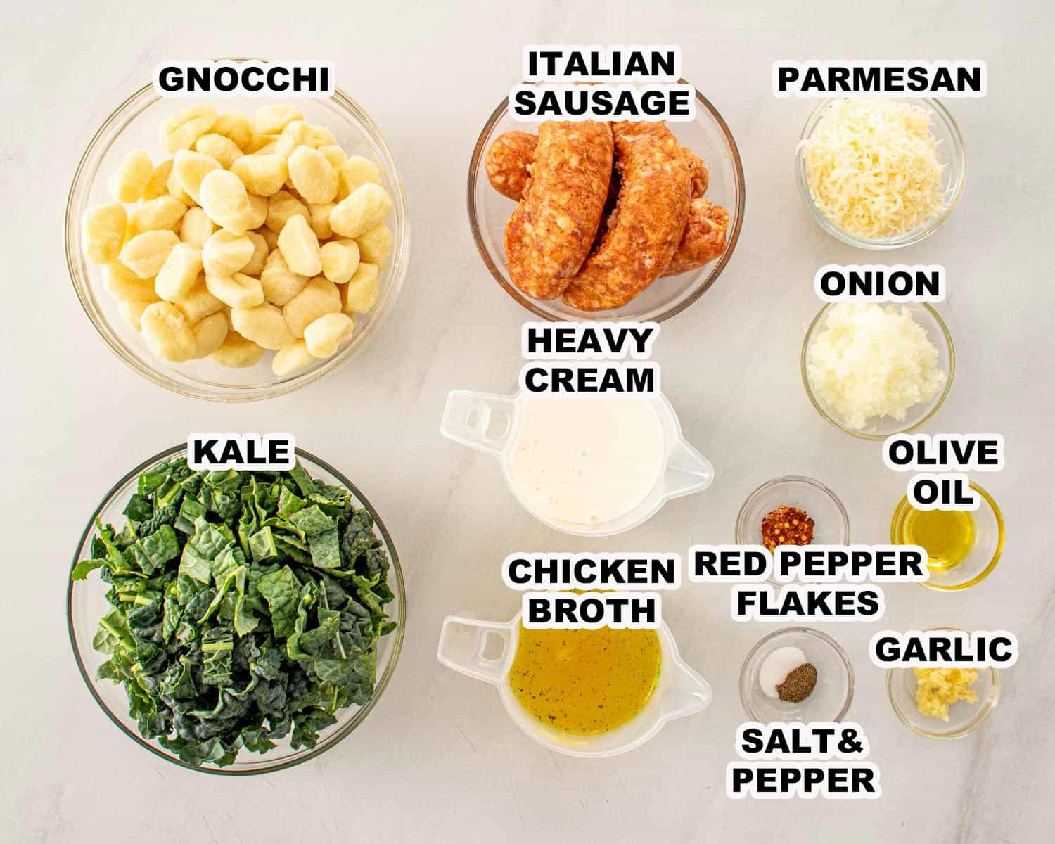 Ingredients for skillet gnocchi with sausage and kale including gnocchi, Italian sausage, kale, cream, broth, garlic, onion, and Parmesan.